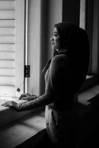 Side view of woman sitting on window at home