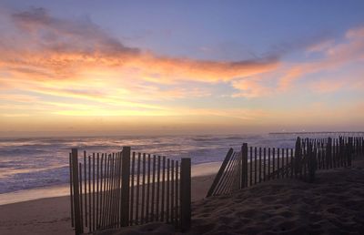 Wooden posts on beach against sky during sunset