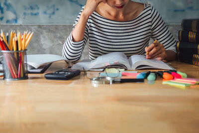 Midsection of woman reading book while sitting on table at home