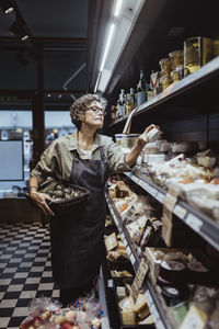 Female owner arranging product on rack at delicatessen store