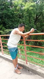 Side view of young man standing against trees