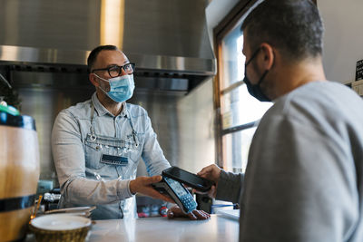 Waiter looking at male customer paying through smart phone at a bar