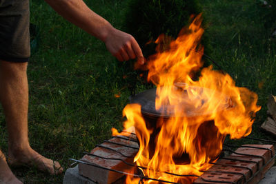 Close up of human hand holding fire flame. man cooking fish soup in the iron bowler over a campfire.