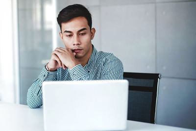 Young man looking away while sitting on table