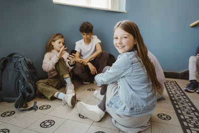 Portrait of smiling girl sitting on floor with friends in school