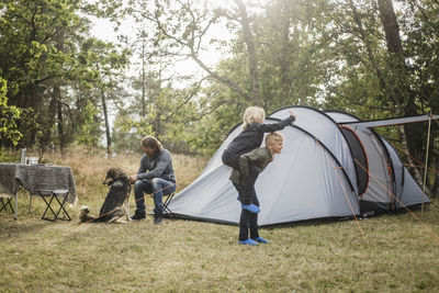 Siblings playing while man sitting with dog by tent at camping site