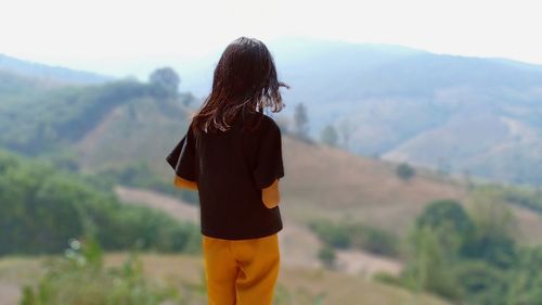 Rear view of teenage girl standing against mountains