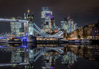 Illuminated modern buildings by river against sky at night