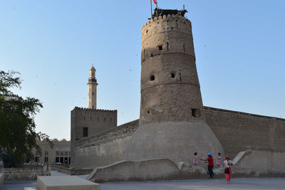 People walking in front of historical building against clear sky