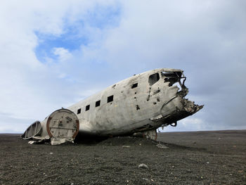 Abandoned airplane on field against cloudy sky