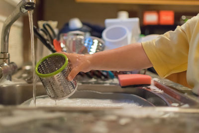 Boy washing container at kitchen sink