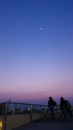 Silhouette people at sea against clear sky at sunset