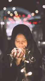 Teenage girl holding illuminated string lights at night