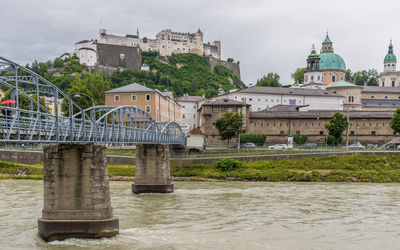 Arch bridge over river by buildings against sky