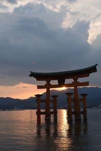 Gazebo on sea against sky during sunset