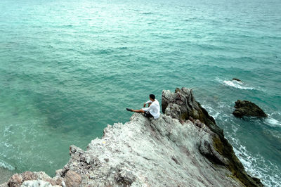 High angle view of men sitting on rock by sea