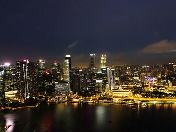 Illuminated buildings by river against sky in city at night