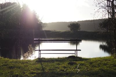 Bench by lake against sky