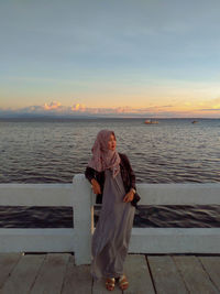 Woman standing by sea against sky during sunset