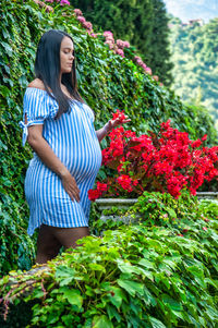 Gorgeous pregnant south american girl, wearing a long striped shirt and observing a flower