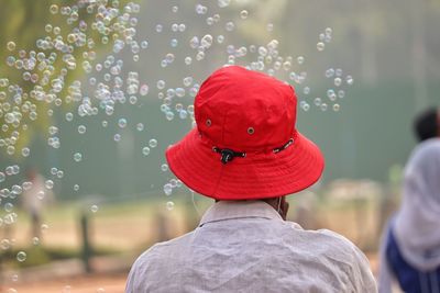 Rear view of man wearing red bucket hat with bubbles in mid-air