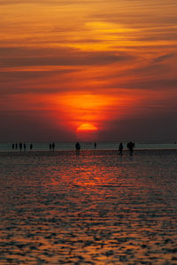 Silhouette people on beach against orange sky