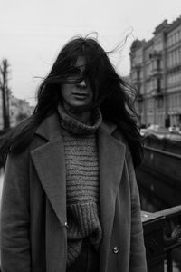 Portrait of woman with long hair standing against sky in city