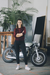 Portrait of confident female entrepreneur standing against motorcycle in creative office