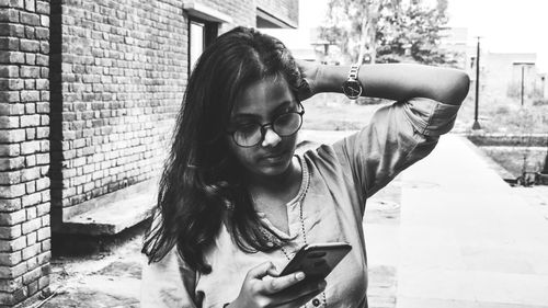 Young woman using mobile phone while standing against wall