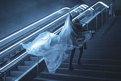 Rear view full length of young woman holding plastic on steps