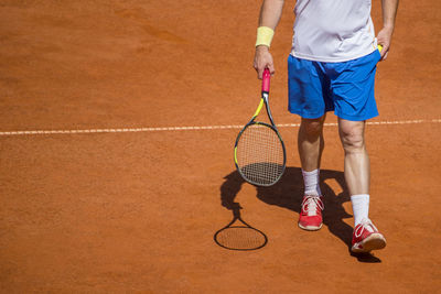 Low section of man with racket walking at playing field