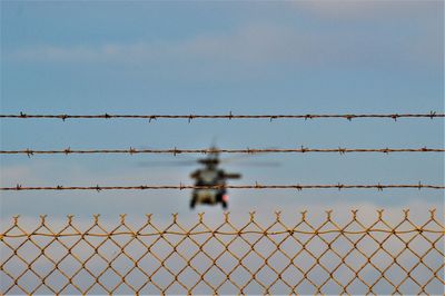 Chainlink fence against clear sky with helicopter
