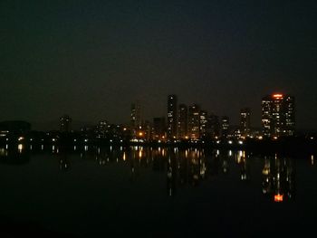 Illuminated buildings by river against sky at night