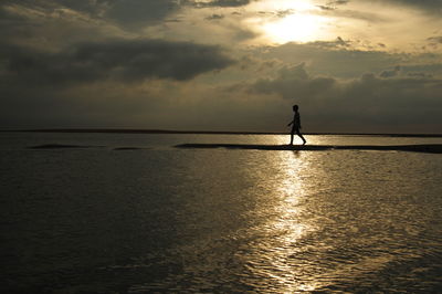 Silhouette man standing on shore against sky during sunset