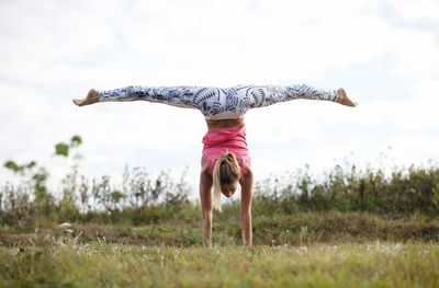 Full length of woman performing handstand on field against clear sky