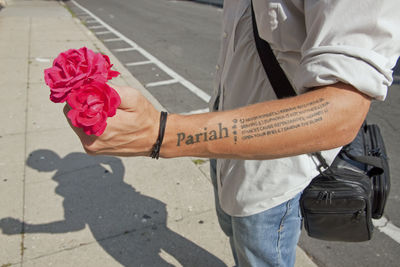 Midsection of man with tattoo holding roses on sidewalk