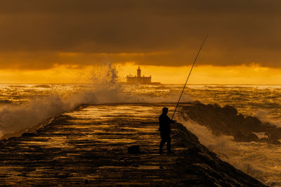 Silhouette man fishing in sea against sky during sunset