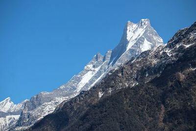 Low angle view of snowcapped mountains against clear blue sky