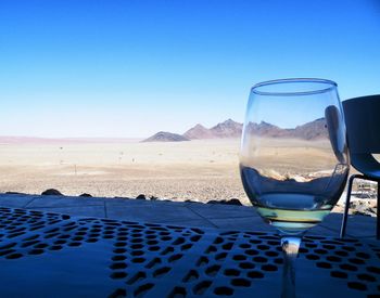 Close-up of beer on table at beach against clear blue sky