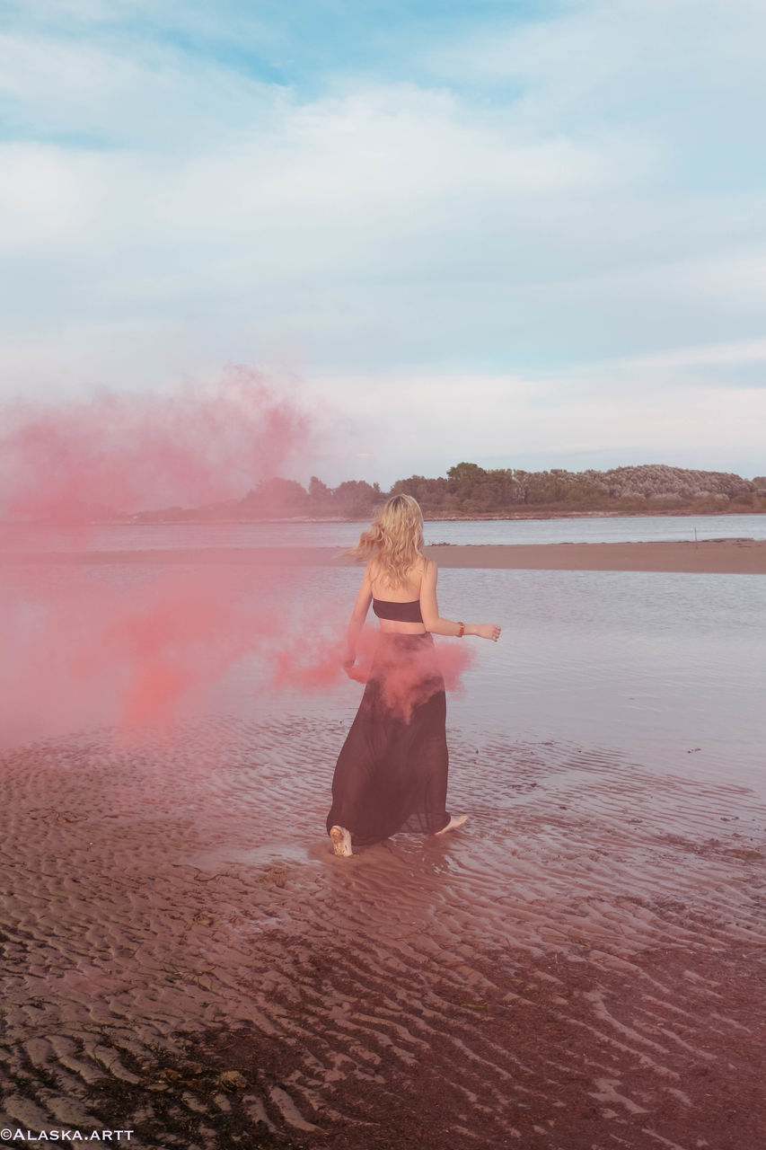 REAR VIEW OF WOMAN STANDING ON BEACH