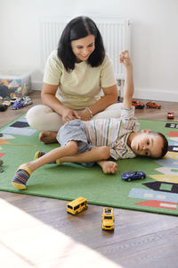 Disabled boy playing toy cars with mother at home. cerebral palsy child entertaining on the mat with