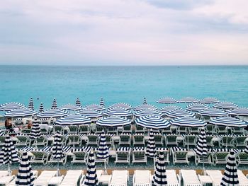 Deck chairs and parasols arranged by sea against sky