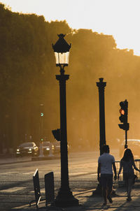 Rear view of couple walking by gas light on sidewalk during sunset