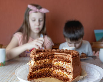 Children girl and boy are sitting at the kitchen table and eating chocolate cake.