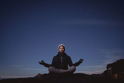 Young man meditating on mountain against sky