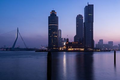 River by illuminated buildings in city against sky at dusk