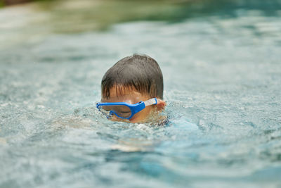 Kid head with goggles in diving down from surface into under water in the sea