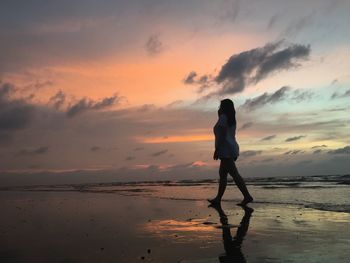 Silhouette woman walking on beach against sky during sunset