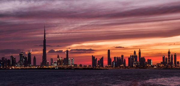 Sea by buildings against sky during sunset