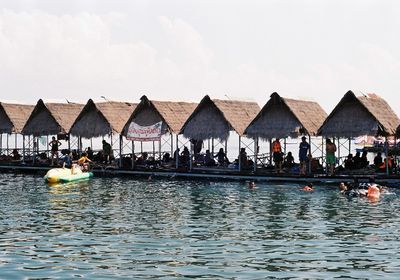 People sitting on deck chairs by sea against sky